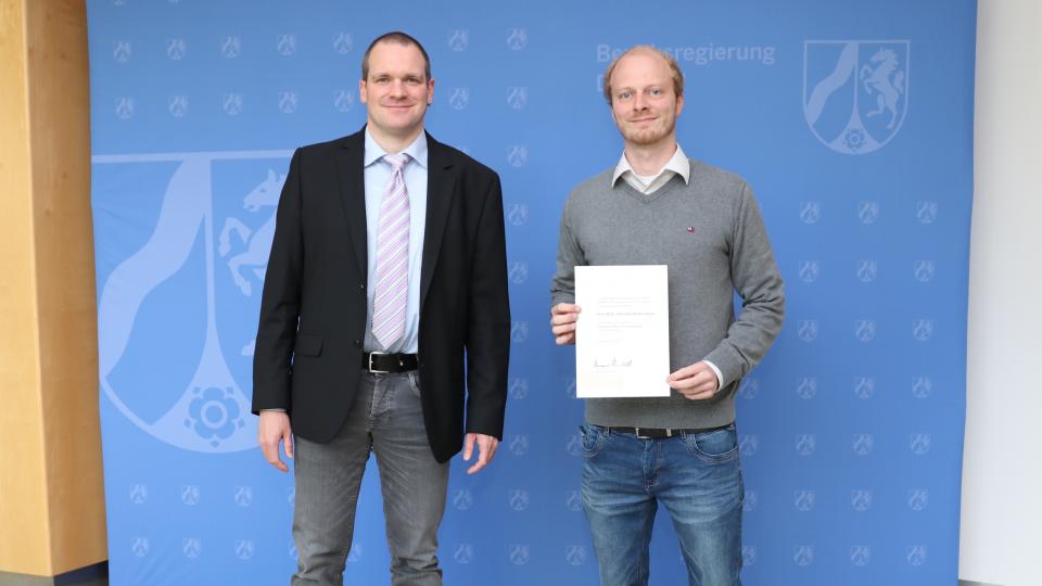 Dezernent Jerome Dutell (links, Bezirksregierung Detmold) überreichte Falko Klasen die Bestellungsurkunde zum Öffentlich bestellten Vermessungsingenieur (ÖbVI).